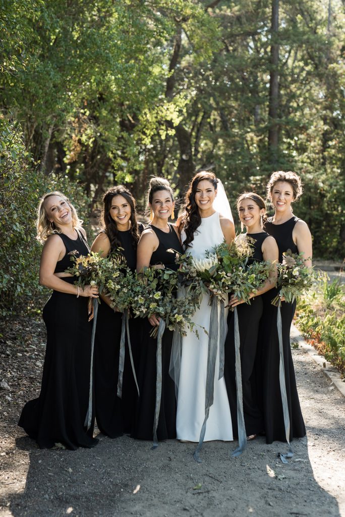 bridesmaids wearing black jumpsuits and greenery bouquets